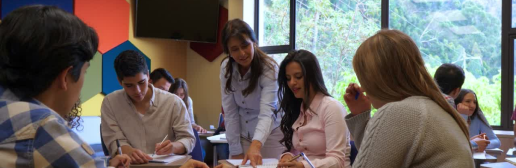 A group of students at a table and a teacher helping them.